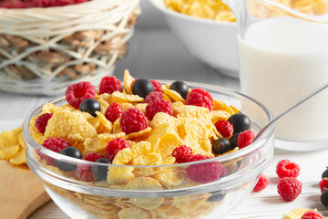 Glass bowl with cereal flakes and berries and milk on the table, close-up. Healthy summer breakfast