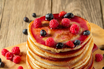 Stack of pancakes with syrup and fresh berries on wooden board on table