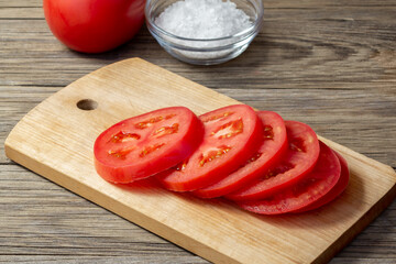 Tomato sliced into round slices on a wooden cutting board