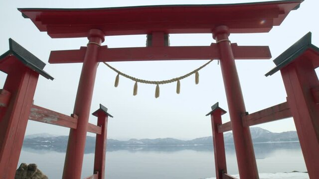 Traditional japanese gate near a mirror-like reflective crater-lake. A sacred torii gate near the deepest lake in japan, tazawa-lake in akita prefecture