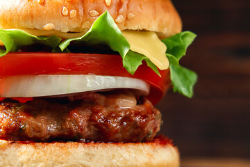 Fresh homemade burger with meat cutlet, tomatoes, lettuce, cheese and onions on a wooden background, close up