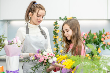 Young woman teaches to young girl arranging flower at flower shop