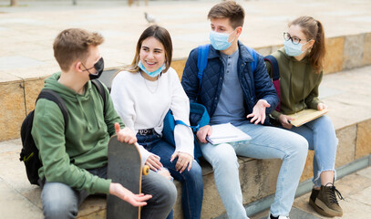 Group of modern cheerful teenagers in protective masks having fun spending time together