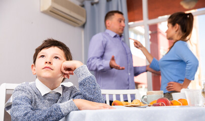 Portrait of unhappy preteen boy sitting at home while parents quarreling..