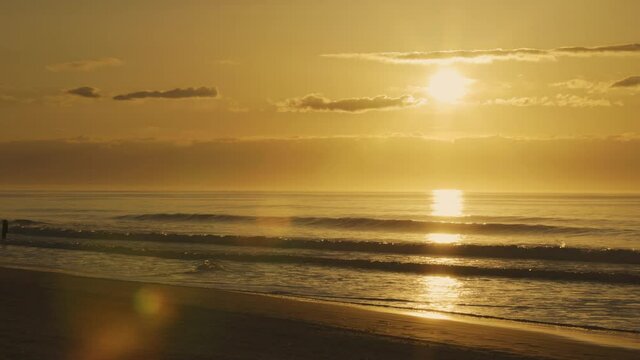 Time lapse shot of golden sunrise with wavy ocean and walking people at sandy beach. North Myrtle Beach,US.