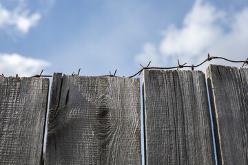 Old fence with barbed wire against the background of a bright blue sky and clouds. Protection...