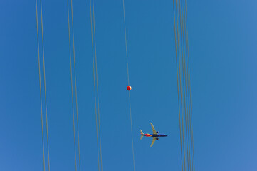 Commercial airplane flies above high-voltage power lines with an aerial marker ball, illustrating aviation safety protocols and overhead utility infrastructure in controlled airspace corridors