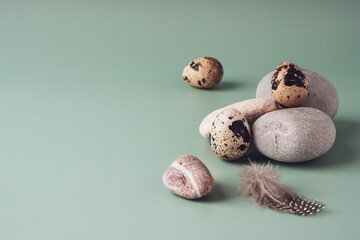 Quail eggs, round stones and feathers lie on a pastel blue background, close-up. Natural modern Easter background. Creative minimalistic Easter concept