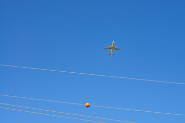 Airplane flying above high-voltage power lines with a visible orange aerial marker, illustrating airspace safety measures near electrical transmission corridors