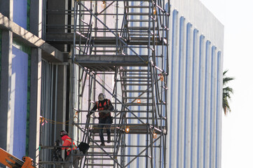 Construction workers wearing safety gear on scaffolding along commercial building exterior,...