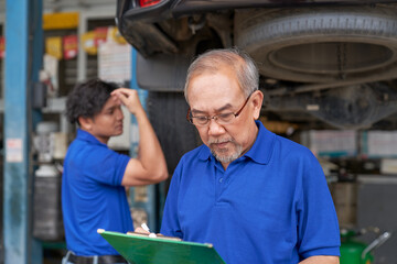 Senior technician and young man check car suspension on hydraulic lift in car garage