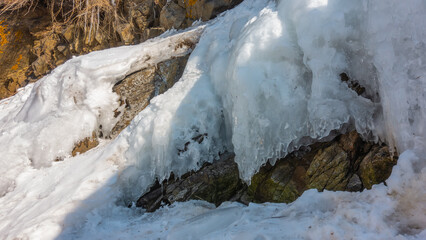 Ice splashes and snow on the rocks. Icicles begin to melt under the rays of the spring sun. End of...