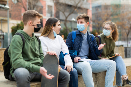 Four teenagers in protective masks are talking about play on walk on the street