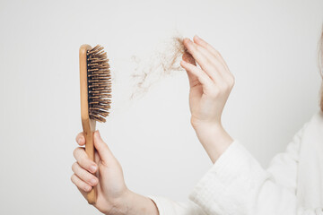 Fototapeta woman removes a bun of hair with a wooden comb on a light background health problems loss obraz