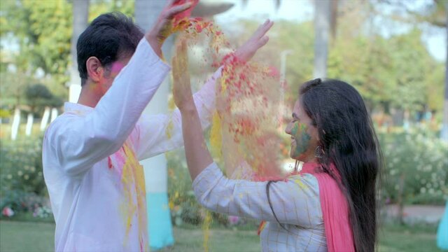 Happy couple applying Gulal on each other during traditional Holi celebration. Two youngsters covered with Abeer celebrating the spring festival of colors together in a garden