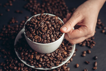 coffee beans In a saucer and in a cup of coffee on a gray background female hand macro photography