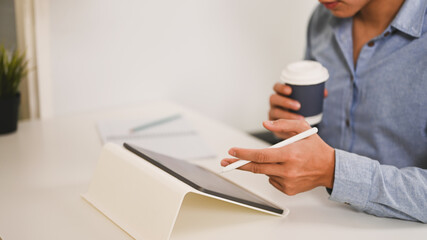 Fototapeta premium Cropped shot of businessman holding cup of hot beverage and working with digital tablet.