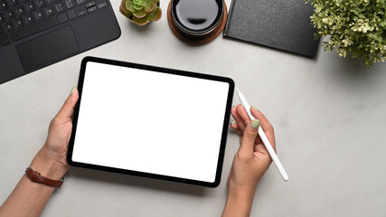Above view of woman holding digital tablet and stylus pen on her office desk. Blank screen for products display montage.