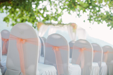 View of chairs in white covers with pink ribbons during a beach wedding