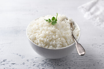 Bowl of cooked white rice on light gray textured background, selective focus, horizontal	