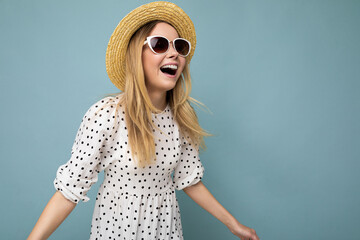 Photo shot of beautiful positive young blonde woman wearing summer casual clothes and stylish sunglasses isolated over colorful background looking to the side