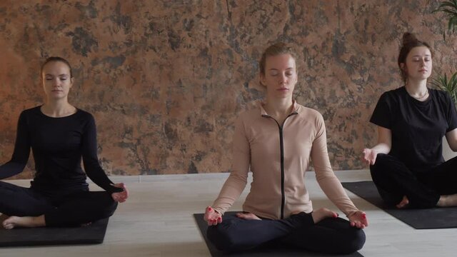 Three young handsome females sitting in studio and making meditation