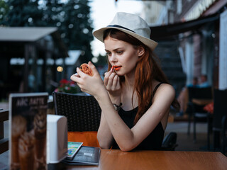 Woman at a table in a cafe with lipstick in hand in a restaurant street