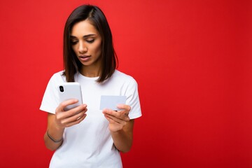 Beautiful young woman wearing casual clothes standing isolated over background surfing on the internet via phone looking at mobile screen