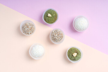 Top view of assortment of nut truffles or homemade sweet energy balls made of coconut, hazelnut, walnut and sesame ingredients laying on trendy colorful pink and orange background. Horizontal image