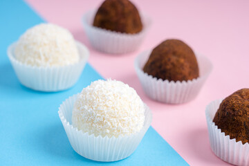 Coconut and cocoa nut truffles or homemade energy balls with a filling of sweetened shredded coconut, condensed milk and curd cheese on colorful pink and blue background. Horizontal, selective focus