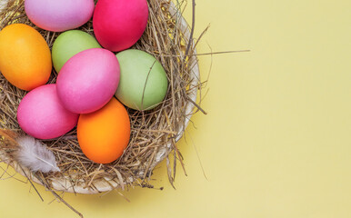 Easter bright eggs in a nest flat lay on a yellow background with a copy of the space