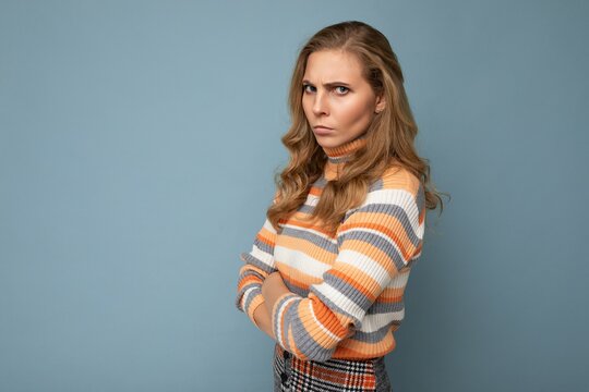 Young pretty beautiful sad upset angry dissatisfied blonde woman with sincere emotions wearing casual striped sweater isolated over blue background with free space