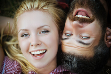 Happy couple in love lying in park, summer holiday romance. Cheerful bearded man and blond girl...