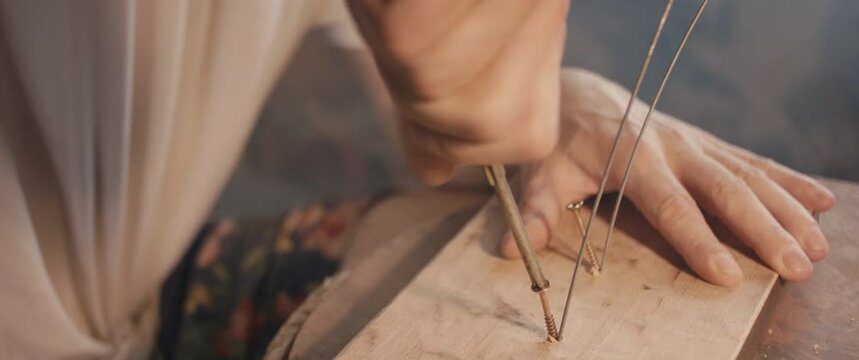 Artist screws wooden sculpture base wire with screwdriver in hand