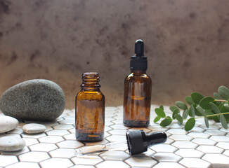 A glass bottle with aromatic oil or serum on a stone and little twig with flowers near. Natural Organic Spa Cosmetic concept. Front view.