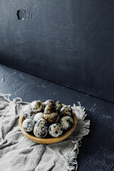 wooden eco bowl full of small spotted quail eggs on dark cement background, isometry is trending in food. stylish card for Easter minimalism. selective focus