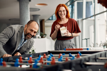 Happy businesswoman watching her colleagues play table football on lunch break in the office.