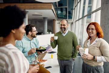 Happy businessman drinking coffee and talking to group of colleagues on lunch break in the office.