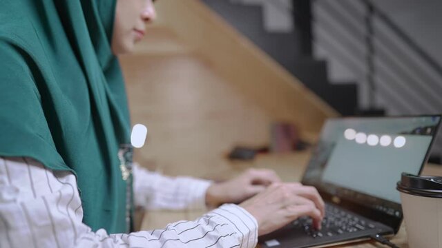 Young muslim working woman wear green hijab using laptop computer doing work research gathering information for master degree final thesis project, modern islam female working at home during pandemic
