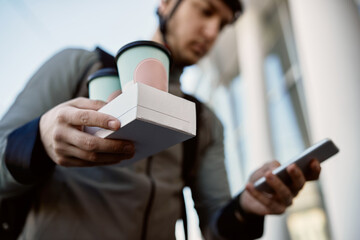 Close-up of delivery man carrying order while checking address on mobile phone.