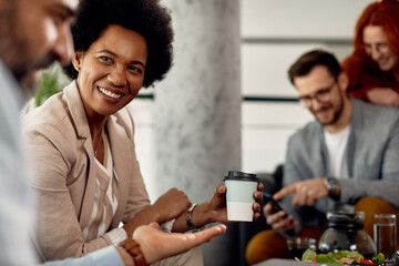 Happy African American businesswoman talking to co-worker and drinking coffee on a break at work.