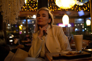 Beautiful woman sit in night cafe and eat fast cafe and dink coffee in evening.