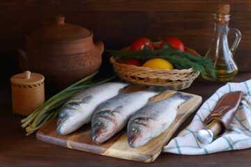 Still life with raw fish sea bass and vegetables before cooking on the dark wooden background. Low key. 