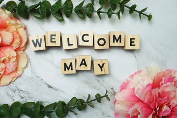 Welcome May alphabet letter with green leave and pink flower flat lay on marble background
