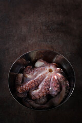 A whole octopus in a metal bowl. Cooking octopus. Photos without people. Dark background. Seafood dishes. Protein food.Vertical photo.