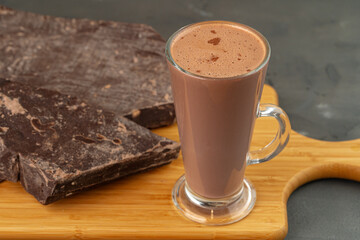 Hot cocoa drink in glass cup and chocolate bar on gray background