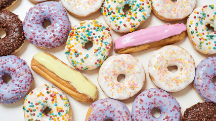 Top view of various delicious sweets, colourful round glazed donuts with sprinkles and eclairs