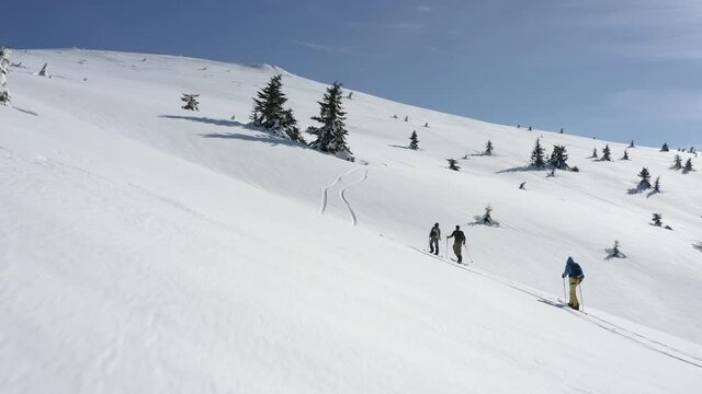 Drone low flight close to three unrecognizable persons climbing mountain on splitboards.