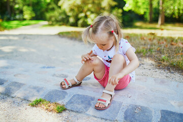 Cute little toddler girl sitting on the ground after falling at summer park