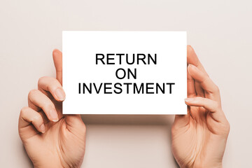 Female hands hold card paper with text Return on Investment on a yellow background. Business and finance concept